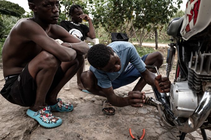 Pelikito 17 anni, ripara la sua motocicletta mentre Tiupi e Alfredo lo guardano lavorare. Batey Lichi Lichima, provincia de La Romana -  Repubblica Dominicana